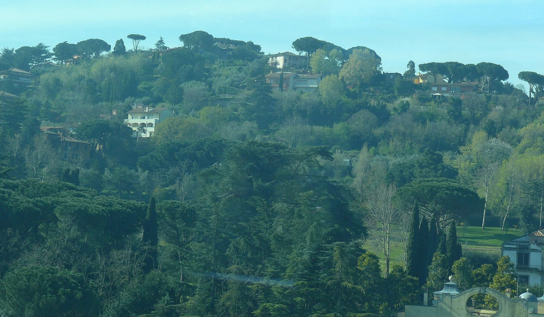 Versante boscoso e case sparse, nella foschia, visti dal finestrino di un treno in Italia